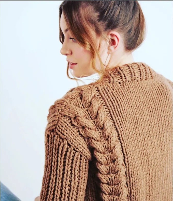 A model in a camel coloured chunky jumper with a bold cable running down the sleeve