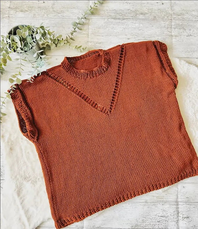 A rust coloured knitted V neck tee with eyelet detail, laid flat with eucalyptus