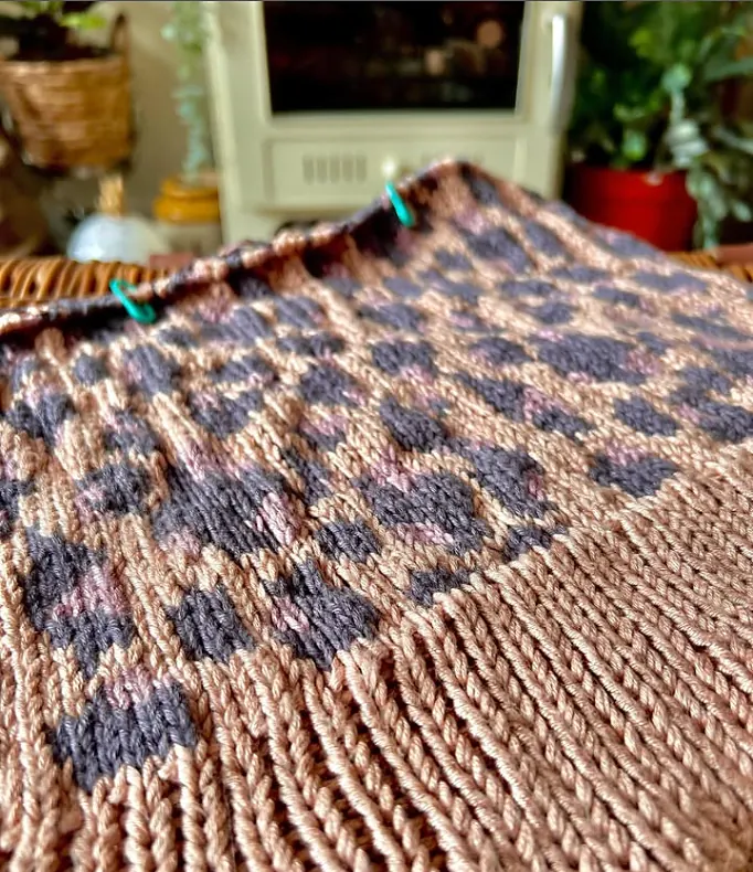 Work in progress: a pink knitted piece with a grey and mauve leopard print colourwork pattern, with stitch markers