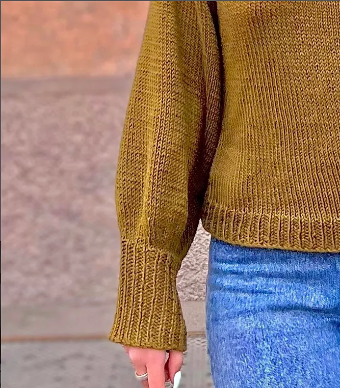 Close up of an olive cotton jumper with long ribbed cuffs, worn with jeans